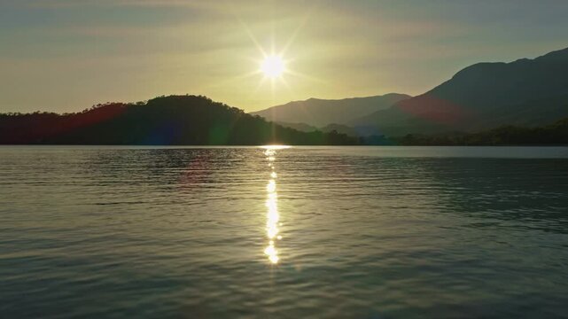 Scenic sunset over a tranquil Phaselis Bay with golden sun reflection on calm water and silhouetted hills in the background - Aerial Wide Angle View
