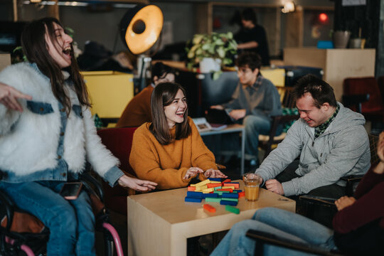 A group of students, including wheelchair users and people with disabilities, laugh while playing a colorful block game at a table.