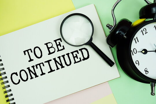 To Be Continued... text written on notepad with alarm clock on pastel background