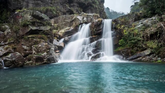 Time-lapse of the silky twin waterfalls cascade through a lush valley, with emerald pools and rocks under soft spring light, Lushan mountain, Jiangxi Province, China.