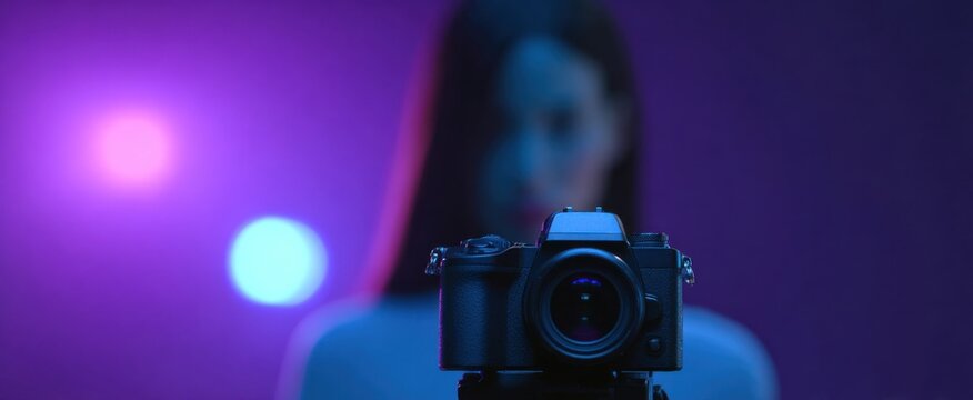 A striking mirrorless camera glows with vibrant blue and purple lights behind a focused photographer.