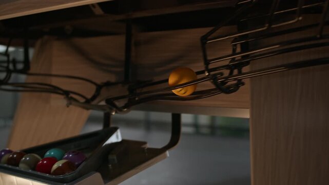 Tracking closeup of billiard ball rolling through internal table return system toward triangle rack, smooth motion showing pool equipment mechanism and gameplay detail