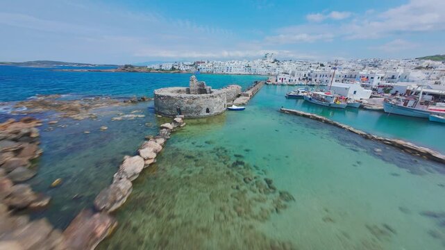 A smooth FPV drone flight over Naousa village on Paros island, Greece, showcasing whitewashed buildings, narrow streets and coastal harbor in bright daylight