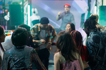 Obraz premium Group of friends holding hands and standing in circle while dancing together in nightclub. Carefree people having fun on crowded dancefloor and partying at disco social gathering in club