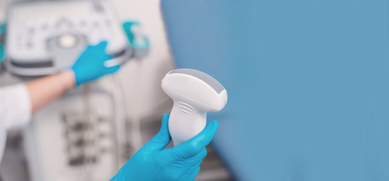 A close-up of an ultrasound machine sensor in a clinic against the backdrop of a doctor's hands. Banner copy space