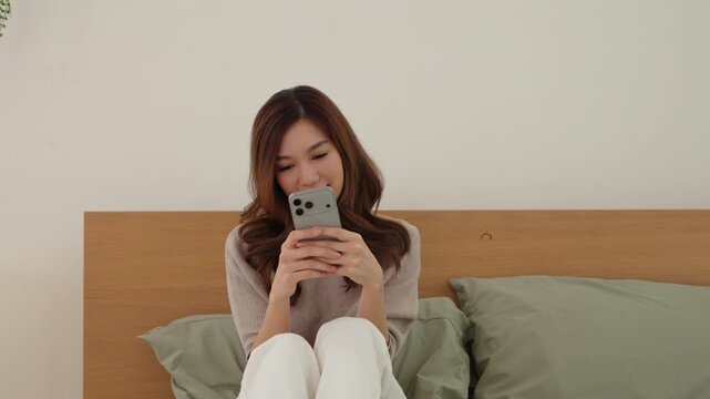 Beautiful Asian woman using smartphone while relaxing in bed