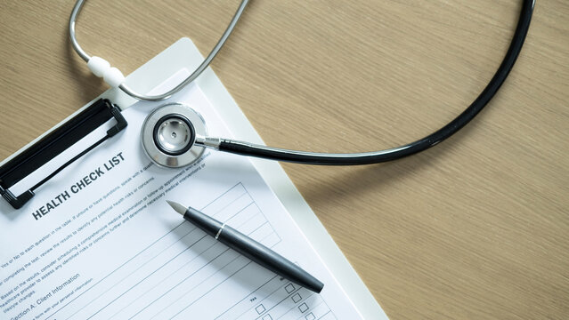Top view of health checklist on clipboard with stethoscope and pen on wooden table, medical screening, patient record and healthcare service concept.