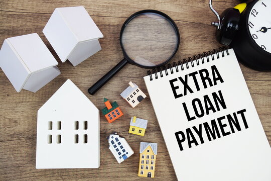 Extra Loan Payment text written on notepad with house model, magnifying glass and alarm clock on wooden background