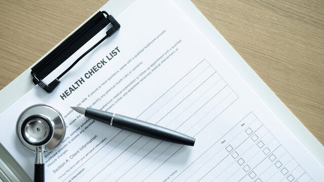 Health checklist document on clipboard with stethoscope and pen on wooden desk, medical checkup, healthcare planning and clinic paperwork concept.