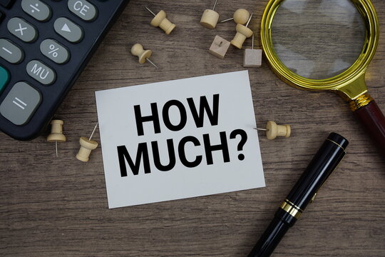 How Much? text written on notepad with pen, alarm clock, magnifying glass and calculator on wooden background