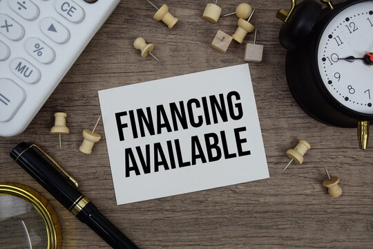 Financing Available text written on notepad with pen, alarm clock, magnifying glass and calculator on wooden background