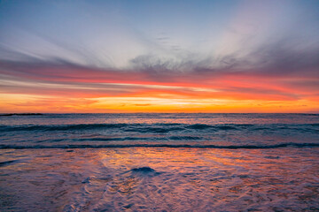 Obraz premium Dramatic Golden sunset over tranquil beach, waves lashing the pebble coastline