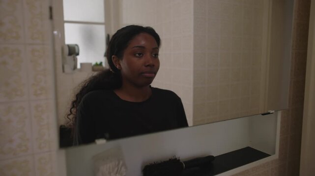 African American woman smiling at her reflection in bathroom mirror after skincare routine creating relaxed and satisfied self care moment in quiet home interior