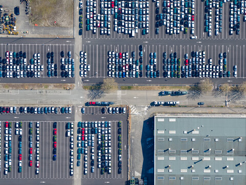 Aerial view of a vast, geometrically arranged car park showcases rows of vehicles in contrasting white, blue, and red hues, punctuated by the stark lines of architecture, Sausheim, Grand Est, France.