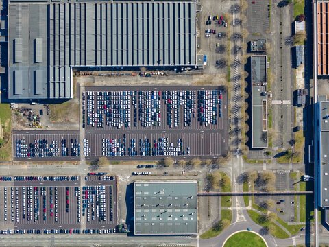 Aerial view of densely packed cars in orderly rows, contrasting with the surrounding industrial architecture, Sausheim, Grand Est, France.