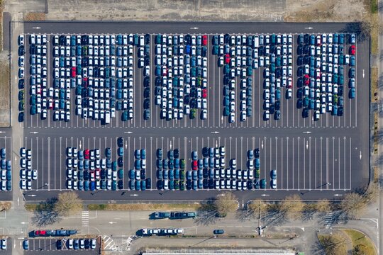 Aerial view of a vast parking lot filled with orderly rows of gleaming cars under the bright sky, the geometric patterns creating a mesmerizing urban landscape, Sausheim, Grand Est, France.
