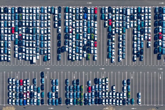 Aerial view of tightly packed cars forming a grid of color and texture, with rows of white lines creating stark contrast against the asphalt, Sausheim, Grand Est, France.