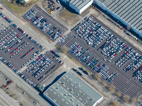 Aerial view of orderly rows of parked cars gleaming under the sun amidst the industrial landscape, Sausheim, Grand Est, France.