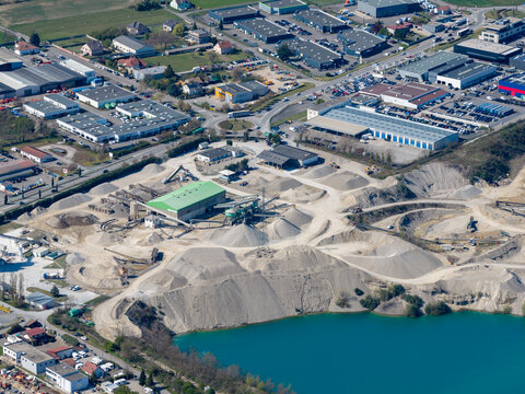 Aerial view of an industrial area with a quarry and a bright blue lake, contrasting with the surrounding buildings, Sausheim, Grand Est, France.