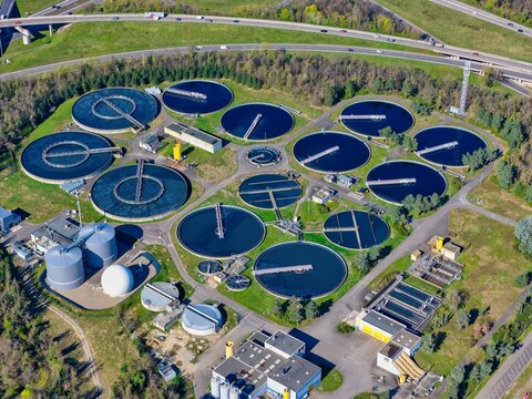 Aerial view of the stark contrast between the dark circular water treatment pools and verdant fields, framed by a highway, Sausheim, Grand Est, France.