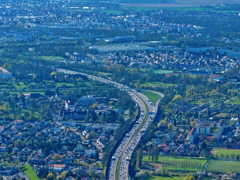 Aerial view of a highway cutting through the urban sprawl, flanked by vibrant buildings and lush greenery, Sausheim, Grand Est, France.