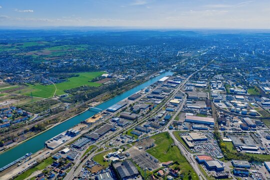 Aerial view of the shimmering Canal du Rhone au Rhin cuts a tranquil path through the urban and industrial sprawl, contrasting with the lush green fields beyond, Sausheim, Grand Est, France.