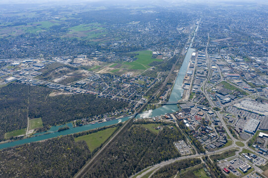 Aerial view of a canal cutting through the landscape, contrasting with the surrounding greenery and urban sprawl, Sausheim, Grand Est, France.