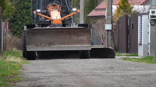 A grader clears a road. Heavy equipment smooths an uneven village road; roadworks. Road paving work, heavy equipment at work.