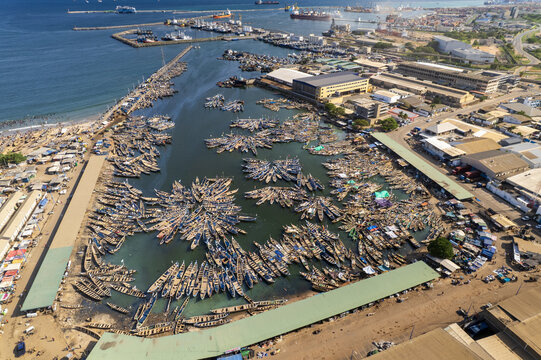 Aerial view of boats clustered in the harbor, casting long shadows on the water against the backdrop of the industrial buildings, Tema, Ghana.