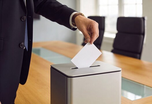 Businessman in suit casting ballot by inserting paper into metal box in boardroom, voting decision and corporate governance concept