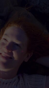 Vertical video: Woman lying on rug smiling as sweeping beam crossing face flares drifting fashion