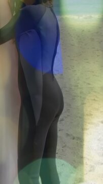 Vertical video: Camera panning up, surfer holding surfboard, preparing for surf amid lens-flare