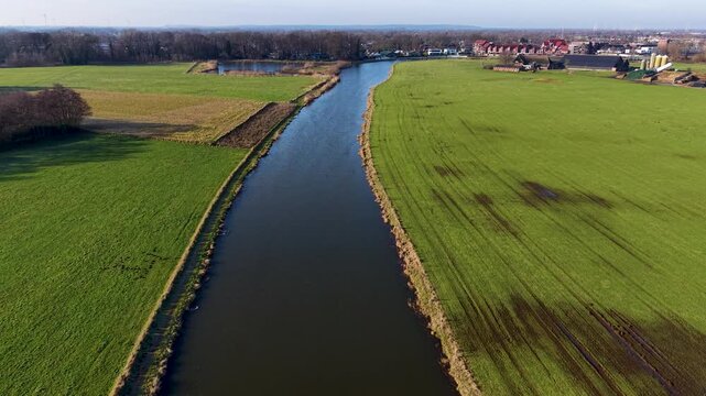 Aerial view of a scenic European river winding through green farmland, alongside a peaceful village featuring a historic brick church with a modern glass nave and houses with solar panels.