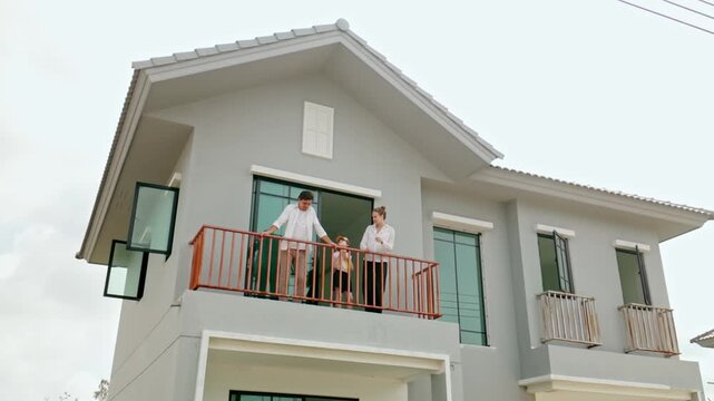 Modern two-story house with gray exterior and large windows; two people stand on the balcony, highlighting clean lines and a calm suburban setting under a bright sky