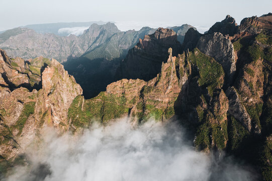 Aerial view of the rugged, sun-kissed peaks pierce through ethereal clouds, creating a dramatic landscape of shadows and light, Pico do Areeiro, Madeira, Portugal.