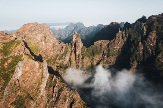 Aerial view of rugged peaks pierce through the clouds, casting long shadows across the dramatic landscape, Pico do Areeiro, Madeira, Portugal.