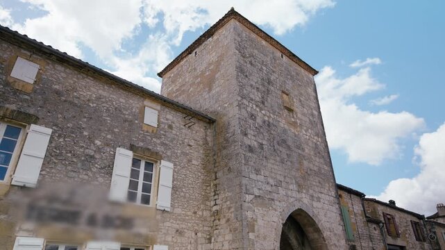 Stone tower and archway of a medieval structure in Monpazier, Dordogne. This scene shows the historic masonry under a cloudy sky. Slow motion travelling shot.