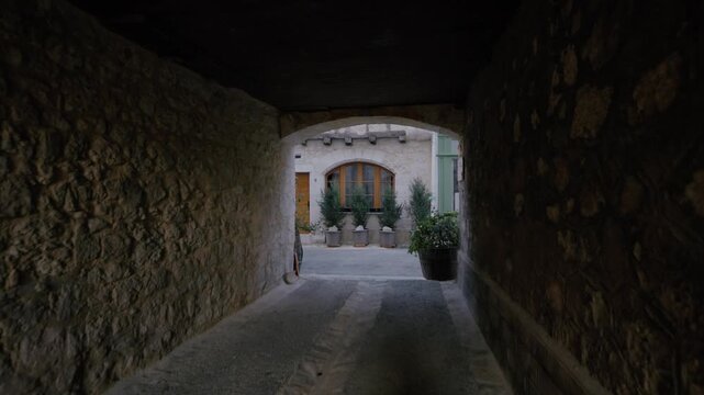 View through a medieval stone archway looking into a quiet courtyard with plants and historic buildings in Issigeac, Dordogne. Static wide shot.