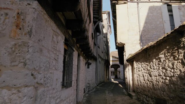 Street-level perspective of a narrow lane winding through ancient stone buildings in the village of Issigeac. Ground-level shot.