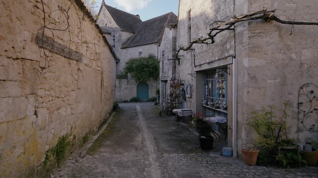 Old French village street featuring stone walls and a charming blue door storefront in Issigeac. Tracking shot through the alley.