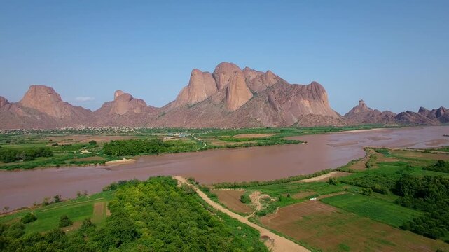 Aerial drone view of Gash River flowing past green agricultural fields toward Taka Mountains in Kassala Sudan, scenic landscape showing nature, terrain and rural environment
