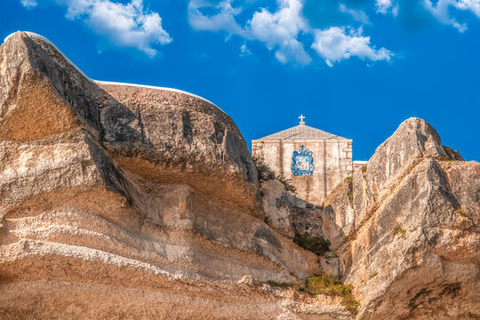 Aerial view of the Chapel of the Miracle's Memory nestled amidst the rugged, sun-kissed cliffs under a vibrant blue sky, Nazare, Leiria, Portugal.