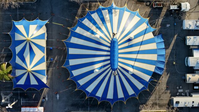 Aerial view of the vibrant blue and white striped circus tents casting long shadows on the asphalt, creating a striking geometric pattern on the ground, St. Augustine, Florida, United States.