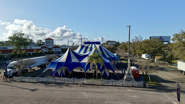 Aerial view of a striking blue and white striped circus tent pitched in a parking lot, contrasting against the surrounding buildings and trees, St. Augustine, Florida, United States.