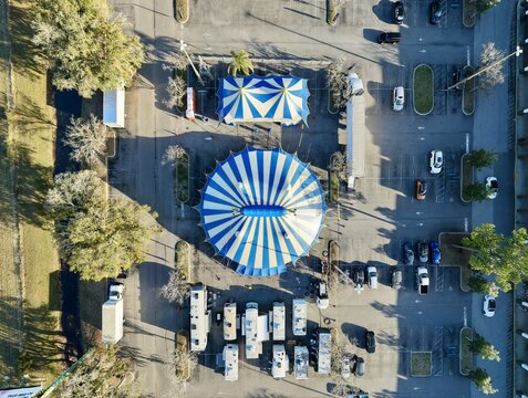 Aerial view of vibrant blue and white circus tents nestled within a sprawling parking lot, surrounded by trees, St. Augustine, Florida, United States.