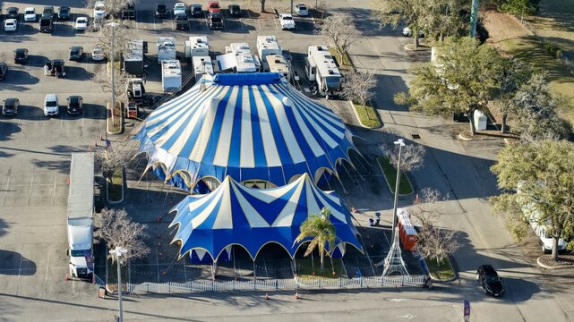 Aerial view of a blue and white striped circus tent rises from a parking lot filled with cars and RVs, creating a vibrant scene, St. Augustine, Florida, United States.