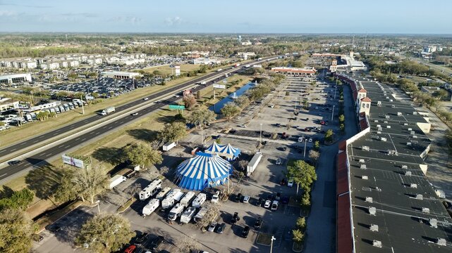 Aerial view of a blue and white circus tent pitched near a highway, juxtaposed against the sprawling parking lot and commercial buildings, St. Augustine, Florida, United States.