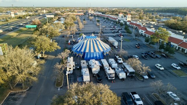 Aerial view of a striking blue and white circus tent standing out against the muted tones of parked RVs and the surrounding urban landscape, St. Augustine, Florida, United States.