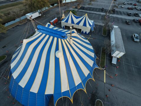 Aerial view of a striking blue and white circus tent pitched against the stark asphalt, a temporary splash of color and wonder, St. Augustine, Florida, United States.