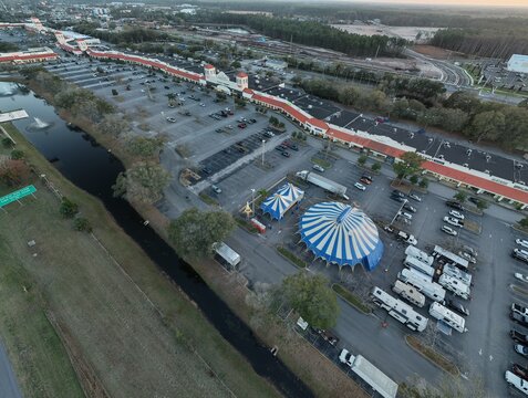 Aerial view of a striking blue and white circus tent amidst a sea of parked vehicles, contrasting with the muted tones of the surrounding landscape, St. Augustine, Florida, United States.